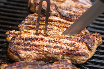 Beef steaks on grill with BBQ fork and knife