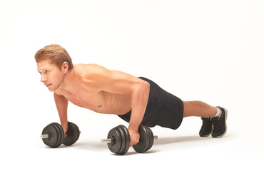 Young muscular sportsman making push-ups on black dumbbells
