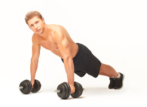 Young muscular sportsman making push-ups on black dumbbells