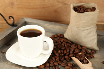 Cup of coffee with beans on tray and rustic wooden background