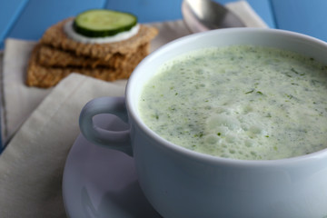 Cucumber soup in bowl on color wooden planks background