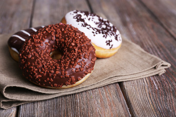 Delicious donuts with icing on napkin on wooden background