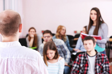 Group of students sitting in classroom and  listening teacher