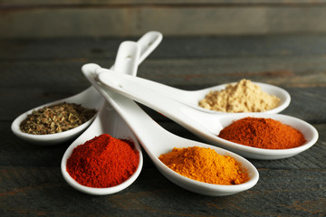 Different kinds of spices in spoons on wooden background