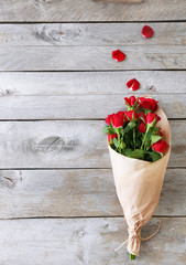 Obraz premium Red roses wrapped in paper on wooden table background