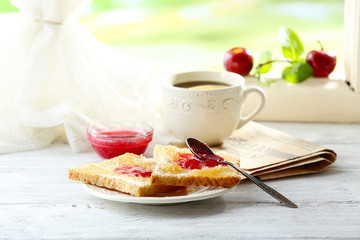 Toasts with jam on plate and cup of tea on bright background