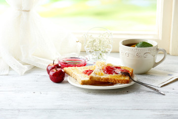 Toasts with jam on plate and cup of tea on bright background