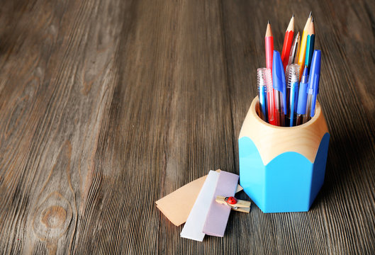 Colorful pens and pencils in cup on wooden table background