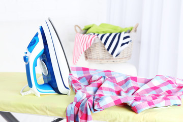 Iron and clothes on ironing board on interior background