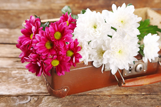 Old wooden suitcase and flowers on wooden background
