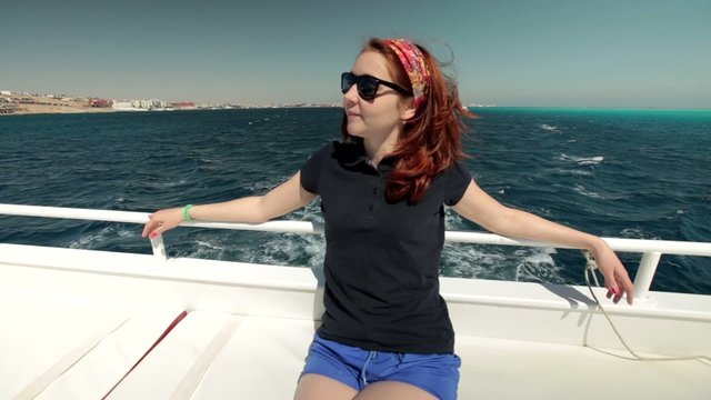 Young happy of life woman in sunglasses sits on a yacht bench of