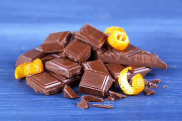 Pieces of chocolate with orange peels on wooden background