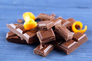 Pieces of chocolate with orange peels on wooden background