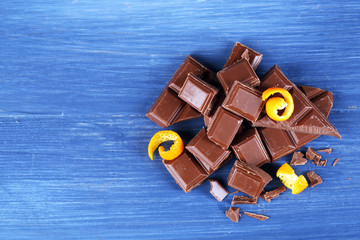 Pieces of chocolate with orange peels on wooden table, top view