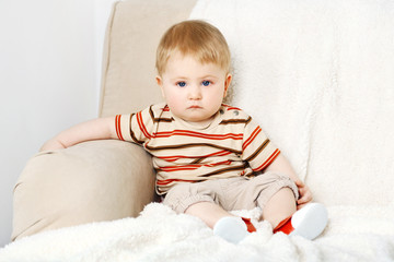 Cute baby boy on sofa, on light background