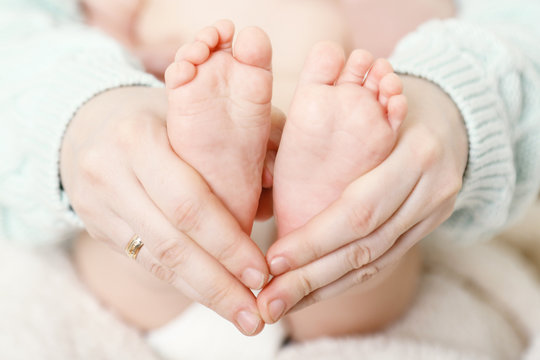 Newborn baby feet on female hands, close-up