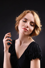 Beautiful young woman with perfume bottle on black background