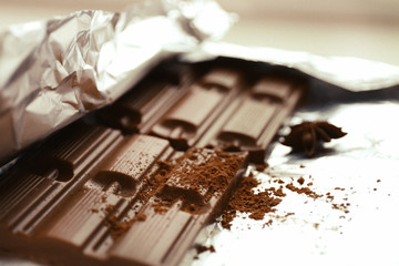 Bar of chocolate with cocoa and star anise on foil, closeup