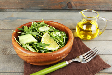 Bowl of green salad and sliced lemon on wooden background