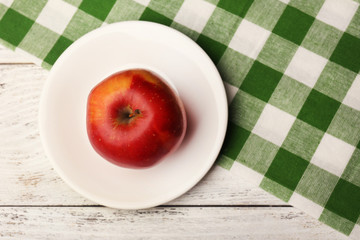 Apple on saucer with napkin on wooden table, top view