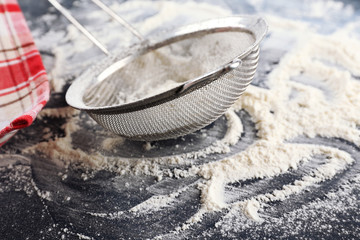 Sifting flour through sieve on wooden table, closeup