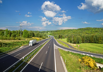 Access road to the asphalt highway between forests. White truck.