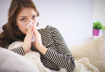 Portrait of a sick woman blowing her nose while sitting on the