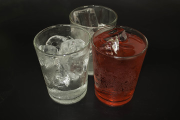Red water and ice in a glass on a black background.