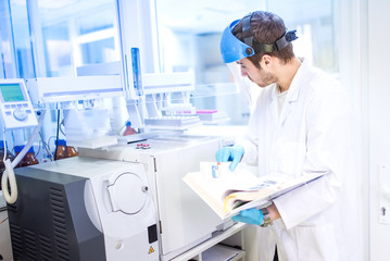 Scientist using manual for chemical computer machinery in lab