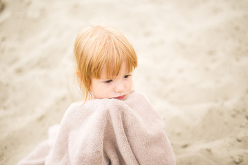 Toddler girl with red hair wrapped in towel at the beach