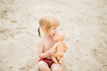 Toddler girl at the beach kissing her baby doll