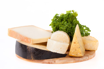 Different types of cheese and a sprig of parsley on a wooden cut