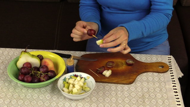 hand string pear dark grape halves on wooden stick on plate