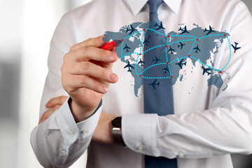Young business man drawing an airplane routes on world map.