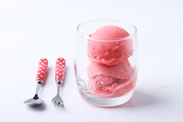 red homemade ice cream scoops in a clear glass with spoon and fo