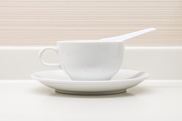 A white ceramic cup with saucer and soupspoon on counter top