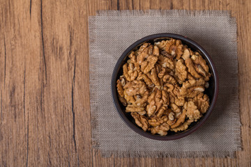 Shelled walnuts in bowl on wooden background