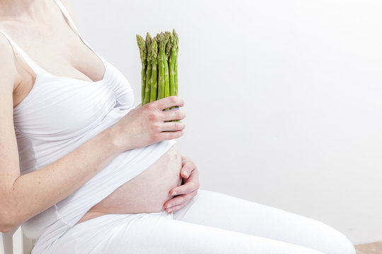 close up of pregnant woman holding green asparagus