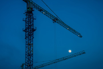 The silhouette of the construction tower canes with the moon