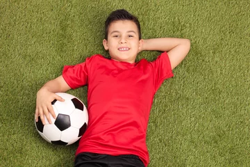 Foto op Plexiglas Relaxed youngster lying on pitch and holding a football © Ljupco Smokovski