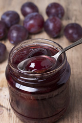 Plum jam in a glass jar and plums on the table.