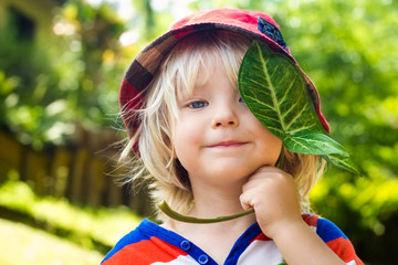 Cute happy child holding a leaf over his eye