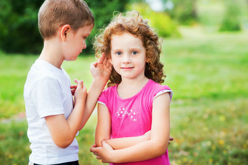 Little boy in white t-shirt whispers a girl in red dress.