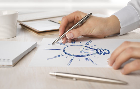 Business woman hand drawing on paper a light bulb