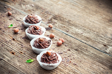 Row of chocolate cupcakes with hazelnuts on top. Wooden backgrou