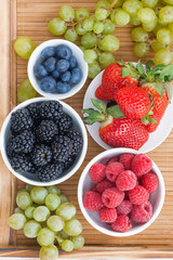 fresh berries in bowl and green grapes on wooden tray, vertical