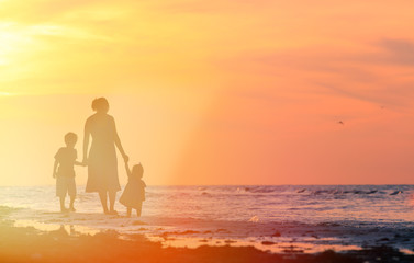 mother and two kids walking on the beach at sunset