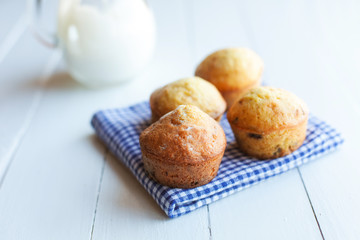 Homemade muffins in blue napkin and jug of milk on wood table. S
