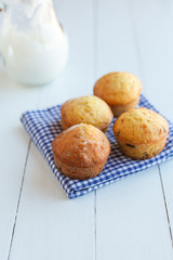 Homemade muffins in blue napkin and jug of milk on wood table. S