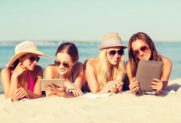 group of smiling young women with tablets on beach